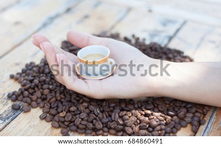 side view of female's hand holding small cup of coffee on coffee grain