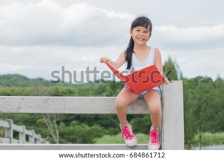 Beautiful smiling teenage girl in White blouse Sitting on a leak and read book, against green of summer park.