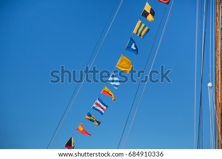 Hanging vibrant colorful nautical marine pattern signal flags spelling message on stretched cable lines on mast of old historic vintage wooden naval maritime war ship boat with blue sky background