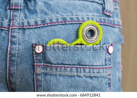 Green fidget spinner in the child's jeans pocket for playing with friends. Closeup. Selective focus.