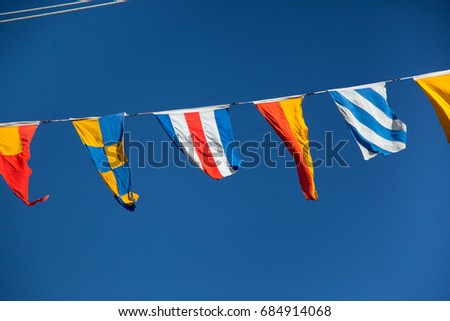 Close up hanging vibrant colorful nautical marine pattern signal system flags billowing on stretched cable lines on mast of old historic vintage wooden naval maritime war ship with blue sky background