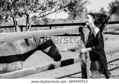 Young beautiful woman with red hair wearing in casual Boho style, with horses on a farm, pets animals in village in a rancho. Horses are human friends