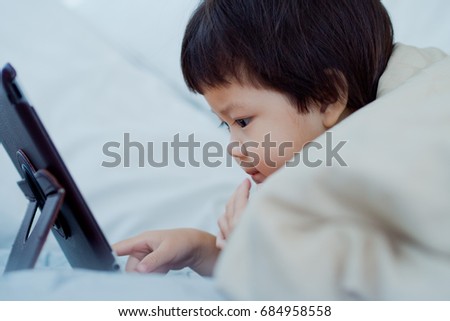 aisan children watching tablet on bed
