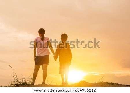 Mother and their son standing holding hands and watching sunset