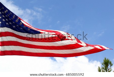 Large U.S. American flag waving in the breeze against a deep blue sky with puffy white clouds on a bright sunny day