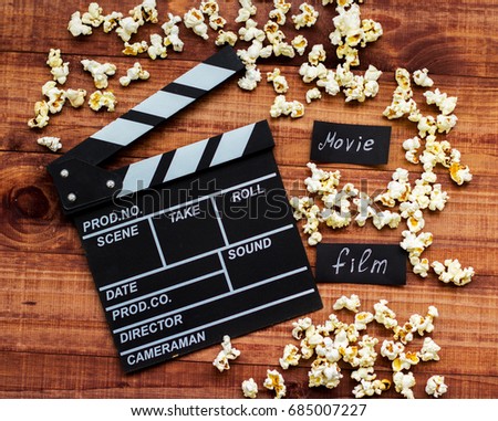 Clapperboard and popcorn on a wooden background with lens flare as a symbol of the film industry, art, filming