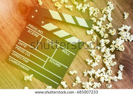 Clapperboard and popcorn on a wooden background with lens flare as a symbol of the film industry, art, filming