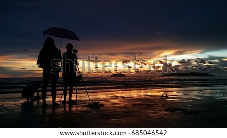 Male photographer and his family taking picture with dslr camera on the beach at sunset time 