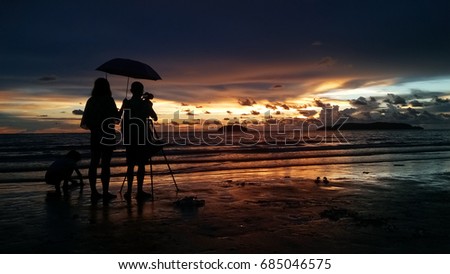 Male photographer and his family taking picture with dslr camera on the beach at sunset time 