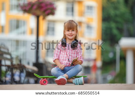 Cool girl with headphones and skateboard in city. Pretty young girl listening to the music and smiling