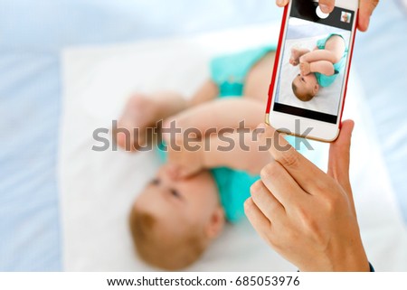 Parent taking photo of a baby with smartphone. Adorable newborn child taking foot in mouth. sucking feet. Digital family memories