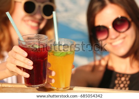 Beautiful young women clinking glasses with cocktails while relaxing in pool, closeup
