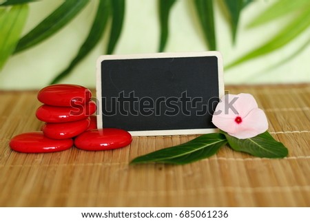 An empty slate to write a message next to red pebbles arranged in zen lifestyle on bamboo wood floor with a peony flower