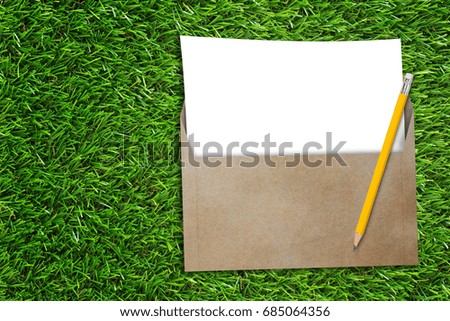 Open business envelope, blank white paper and yellow pencil on green grass background, nature and ecology concept