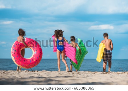 back view of group of kids with inflatable mattresses walking on beach