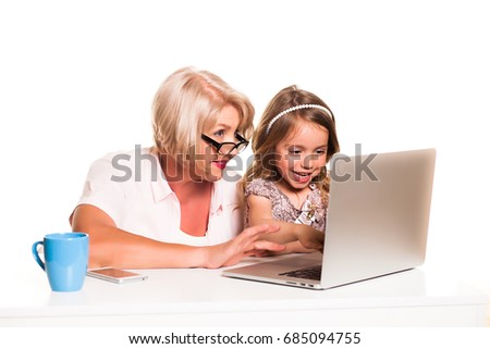 Grandmother and her granddaughter uses laptop together and smiling on white background