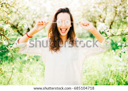 Portrait of young happy cheerful smiling and laughing beautiful brunette cute girl with long hair enjoying summer on vacation in park. Female hiding eyes with two dandelions. Guess who. Invisible life