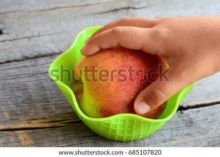 Small child takes a fresh peach in his hand. Sweet juisy peaches on a vintage wooden table. Natural food to support healthy growth and development of child