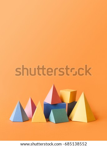 Colorful abstract geometrical composition. Three-dimensional prism pyramid rectangular cube objects on orange paper background. Yellow blue pink green colored solid figures, vertical copy space photo