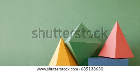 Colorful abstract geometric background with three-dimensional solid figures. Pyramid prism rectangular cube arranged on green paper. Yellow blue pink malachite colored geometrical shapes. Soft focus