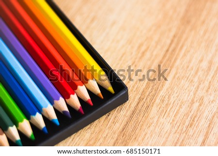Colored pencils in black box on wooden table