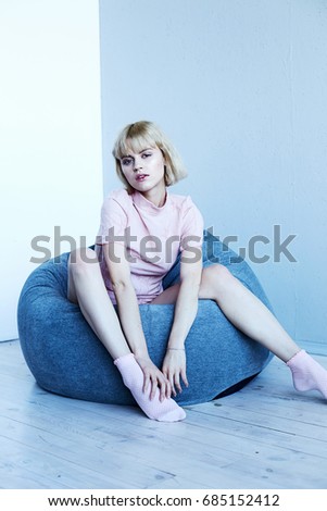 A young girl in a pink home suit near a soft chair. Beautiful model poses for fashion magazine. Picture in calm gray-blue tones. Photo is taken in the studio.