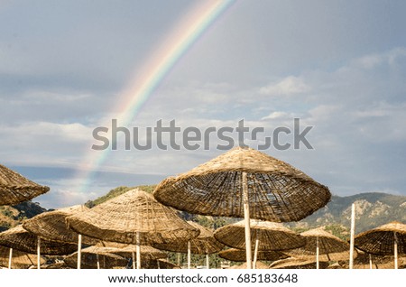 Rainbow in the sky against the background of high rocks and mountains on the beach. Beach umbrellas and skiers on the rainbow background.
