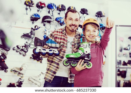 positive american male shop assistant helping boy to choose roller-skates in sports store
