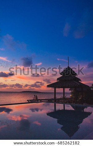Beautiful swimming pool in resort with silhouette couple sit on the wooden bridge in sunset and twilight times.