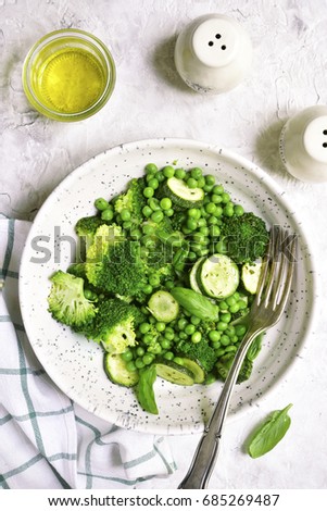 Green vegetables ragout in a clay bowl on a light slate,stone or concrete background.Top view.