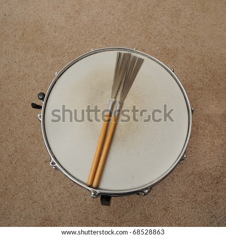 A direct overhead above view of a snare drum on a stand with drum brushes.