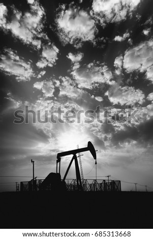 Silhouette of crude oil pump in the oilfield at cloudy sunset - Black and white edit