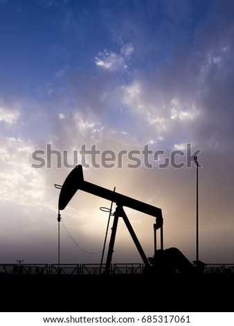 Silhouette of crude oil pump in the oilfield at cloudy sunset 