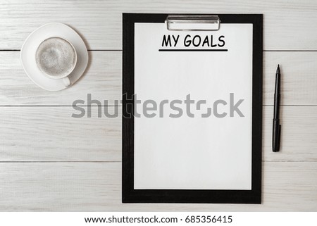 My goals list on note pad paper with pen and coffee on wooden table