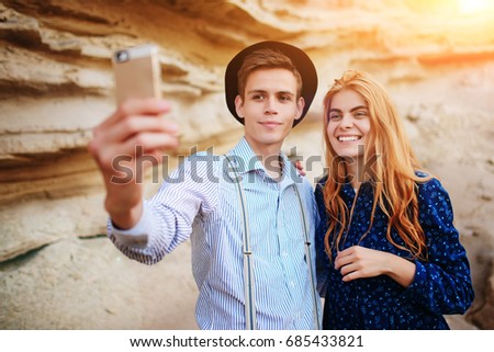 Attractive man with a beautiful woman are hugging and smiling. They are making selfie on the background of sand quarry.