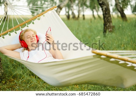 Woman resting in hammock outdoors. Listen to music.