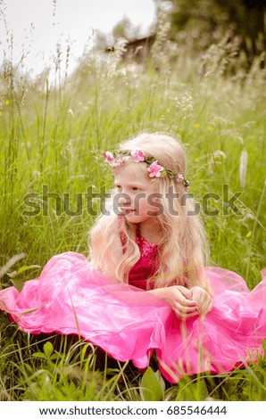 adorable blond girl in pink princess dress sitting in the grass