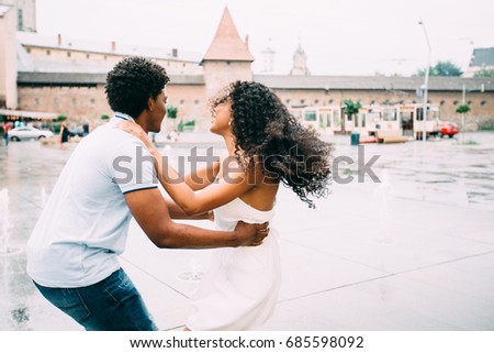 Positive emotional photo of amazing young african american couple whirling and hugging over city square with fountain on background. Travel recreation lifestyle, water fountain.