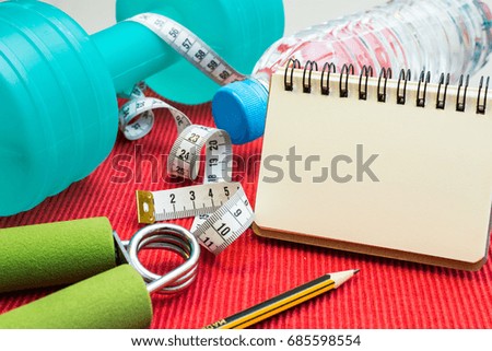 Lay Flat - Dumbbell, Measuring Tape, Hand Grip, Mineral Water, Fresh Apple, Pencil & Blank Notebook for Motivational Quotes/Words on red background - Fitness Concept
