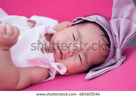 A shot of a cute baby girl with purple headband while sleeping and playing on the pink chair /  Focus at infant girl