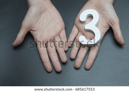 On a black background, female hand with number three.