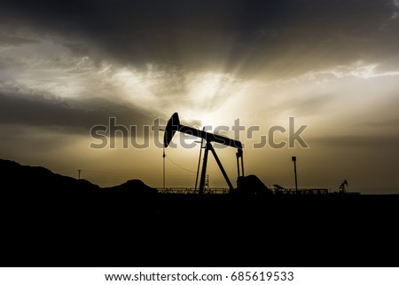 Silhouette of crude oil pump in oilfield at cloudy sunset 