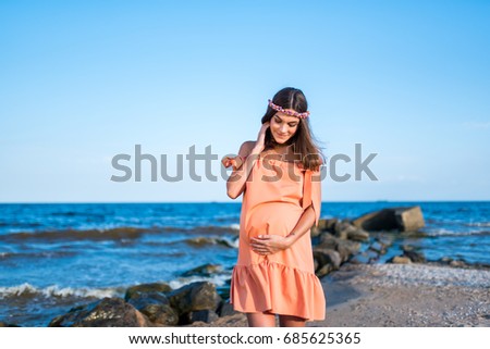 Brown hair pregnant girl in the dress walking on the coast