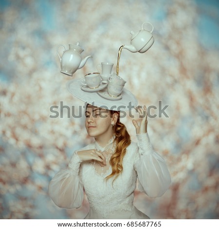 Surreal portrait of a girl in vintage dress with tea cups on her head. Tea time concept
