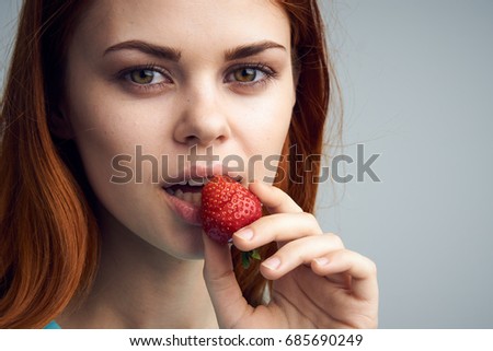 Young beautiful woman on a gray background holds a strawberry.