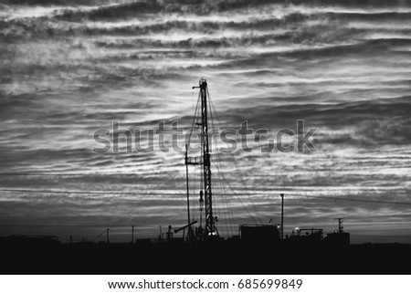 Silhouette or work over rig in the oilfield at cloudy sunset - Black and white edit 