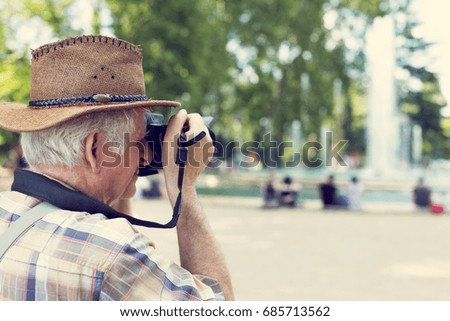 Senior pensioner tourist in hat photographing in vintage style in public city park