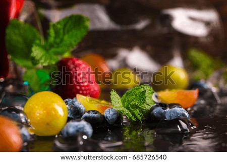 Close picture of sweet colourful berries with mint twigs and chocolate sauce. Ripe yellow grapes, bright sour bilberries and juicy strawberries. Summer fruits for refreshing beverages and desserts.