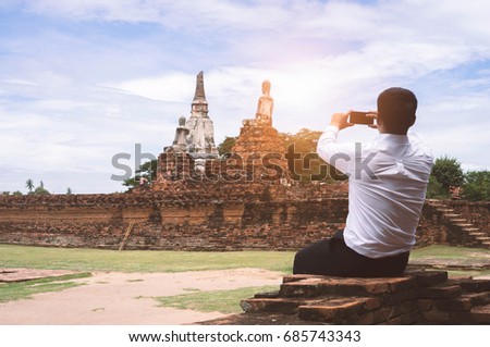 Businessman take a photo of ancient Buddha with smartphone .