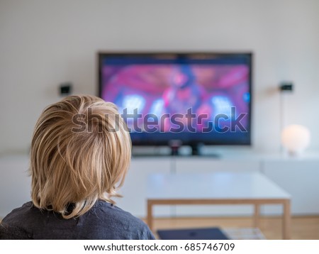 Back view image of cute little blond hair boy sitting on sofa and watching TV.